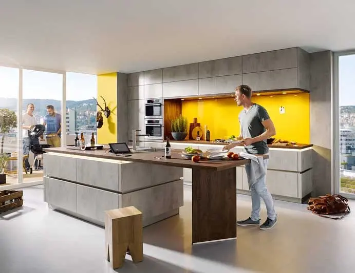 Personen sind in grauer Küche mit Kochinsel und gelber Rückwand am kochen