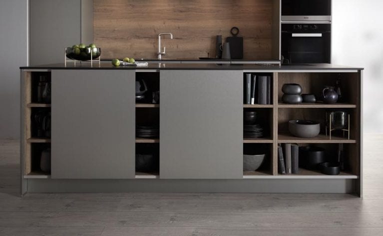 Kochinsel der Contur Küche 53.180 mit Schiebetüren aus geschliffenen Edelstahlfronten und Holzfunier im Hintergrund