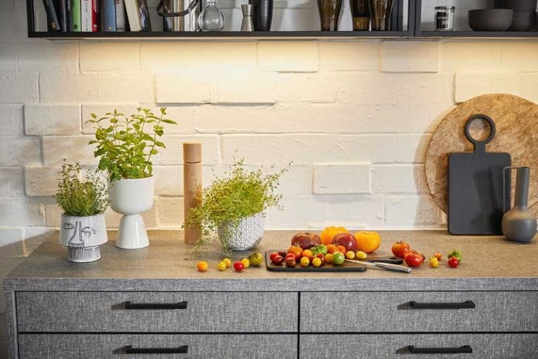 graue Küche mit strukturierter Oberfläche und schwarzen Griffen. Auf der Arbeitsfläche stehen Kräuter und es liegen Tomaten da