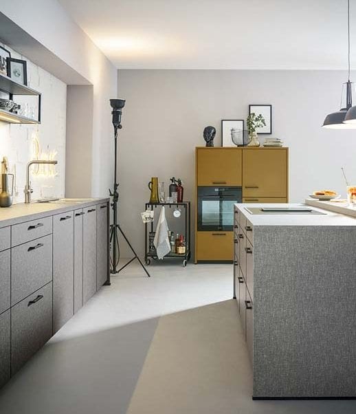 Offene Contur Küche mit Kochinsel in einem strukturierten grau und einem gelben Küchenschrank als Kontrast