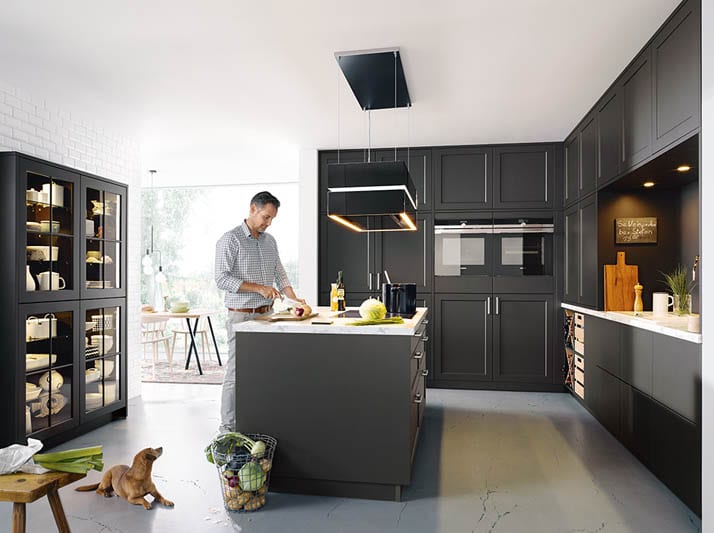 Anthrazotfarbene Conturküche mit grosser Kücheninsel, bei der ein Mann am Kochen ist