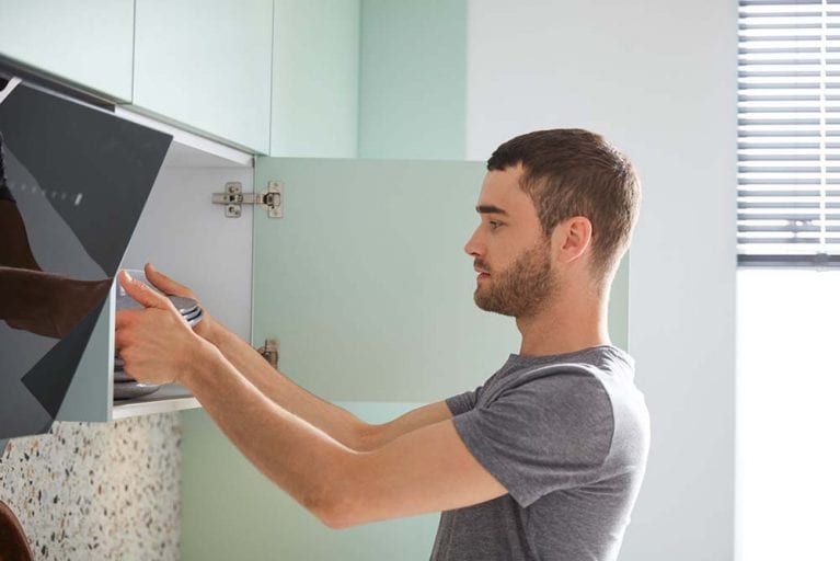 Mann verräumt Teller in mintfarbene Küche von Contur