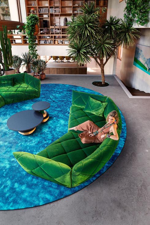 Bretz Sofa in Samtgrün mit Frau in orangenen Jumpsuit darauf