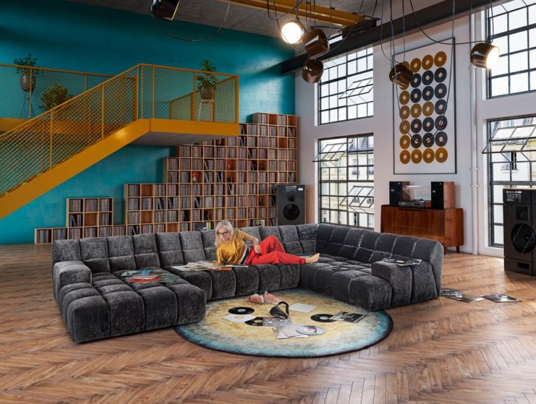 Anthrazitfarbenes Bretz Sofa Ocean7 steht in einem grossen Wohnzimmer mit hohen Decken und eine Frau liest darauf Magazine