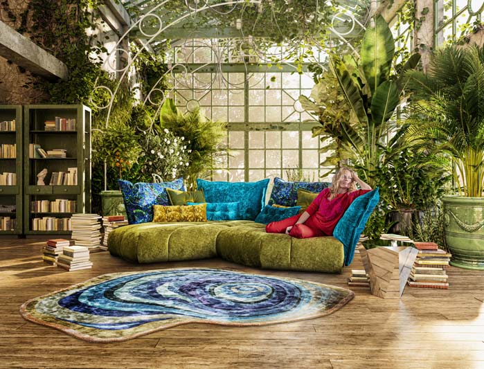 Grün blaues Bretz Sofa Matilda steht in einem gewächshausähnlichem Wohnzimmer mit einer rotgekleideten Blondine darauf.