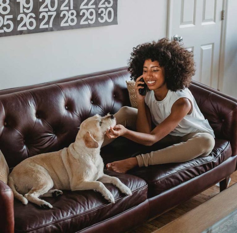 Braunes Ledersofa mit Steppung auf der eine Frau mit Ihrem Hund sitzt.